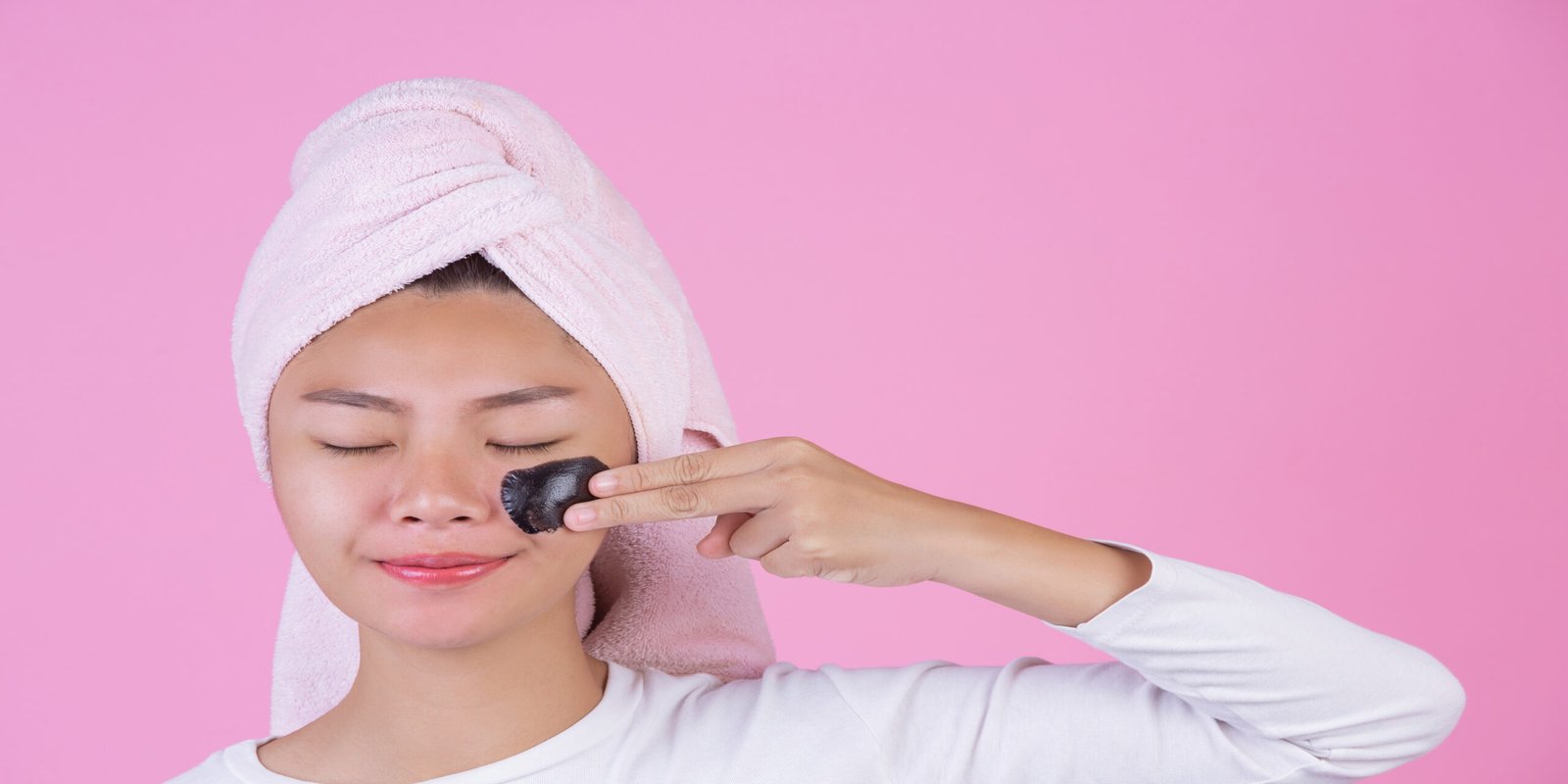 A woman applies a black carbon mask to her cheek, representing the carbon peel treatment benefits for clear and glowing skin.