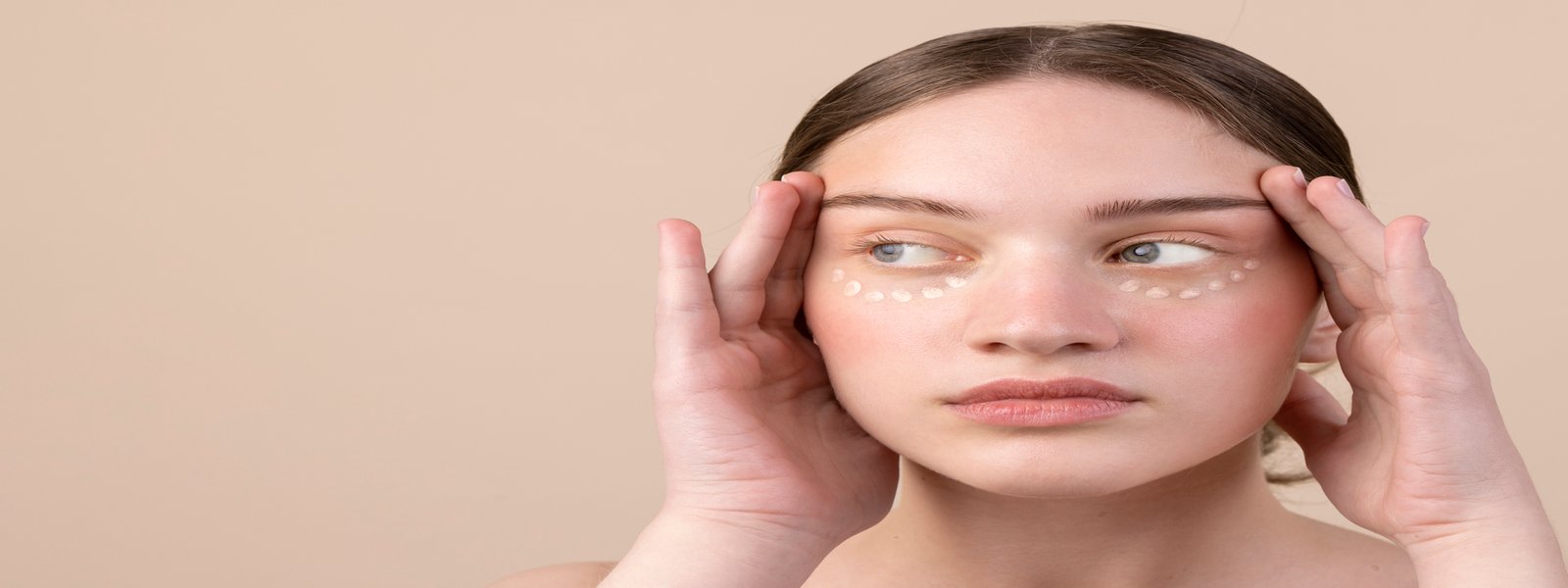 Young woman applying under-eye cream to address dark circles, focusing on self-care and skincare.